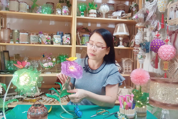 Chị Hoa đang làm sản phẩm tái chế từ chai lọ nhựa, với các mẫu đèn ngủ và hoa