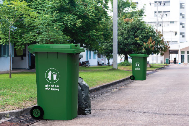 Thùng rác lớn màu xanh đặt tại công viên, góp phần duy trì vệ sinh và khuyến khích ý thức bảo vệ môi trường sống